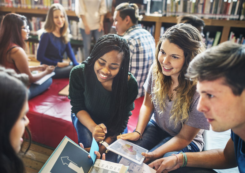 Students gathered around tablet and book in a library