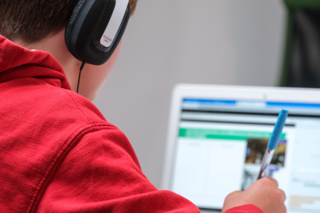 Young student with headphones on taking notes and looking at a laptop