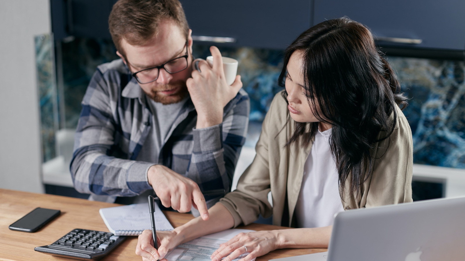 Man and woman sat at a table with a laptop and calculator looking at bills.