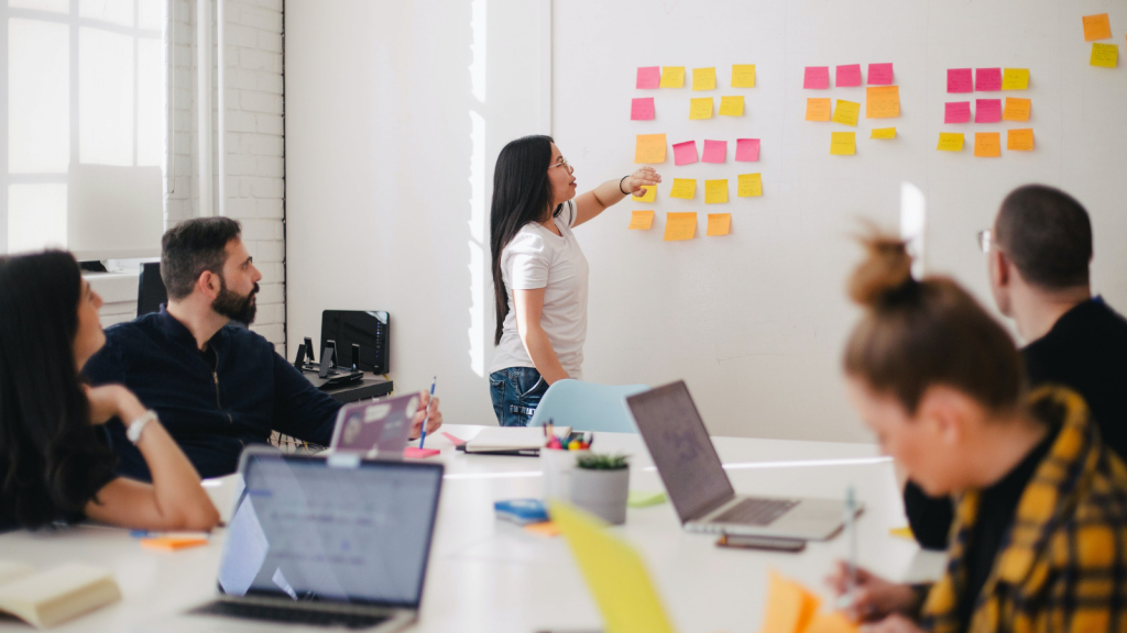 Woman at a whiteboard with postit notes, running a team workshop in a workplace.