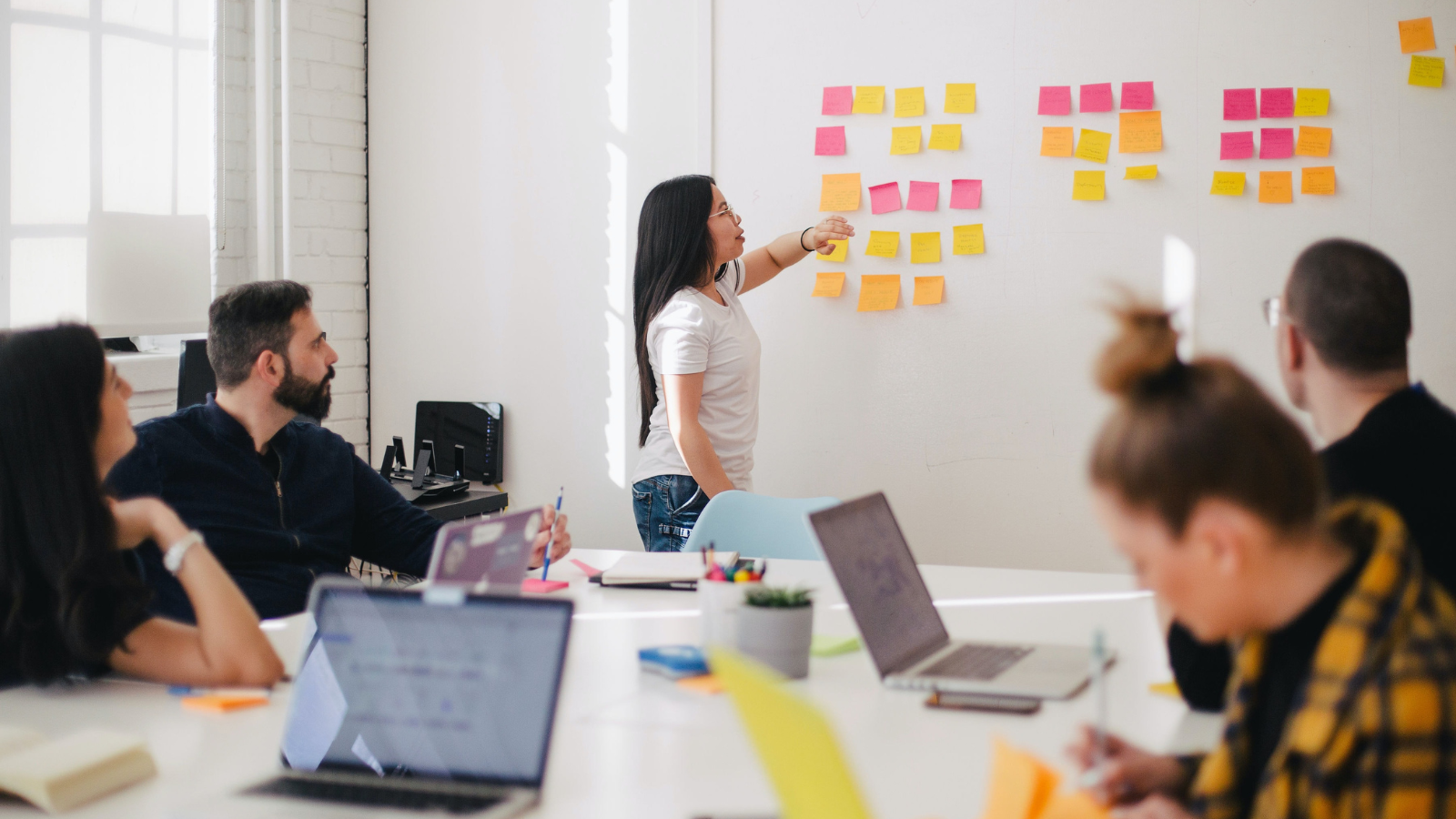 Woman at a whiteboard with postit notes, running a team workshop in a workplace.