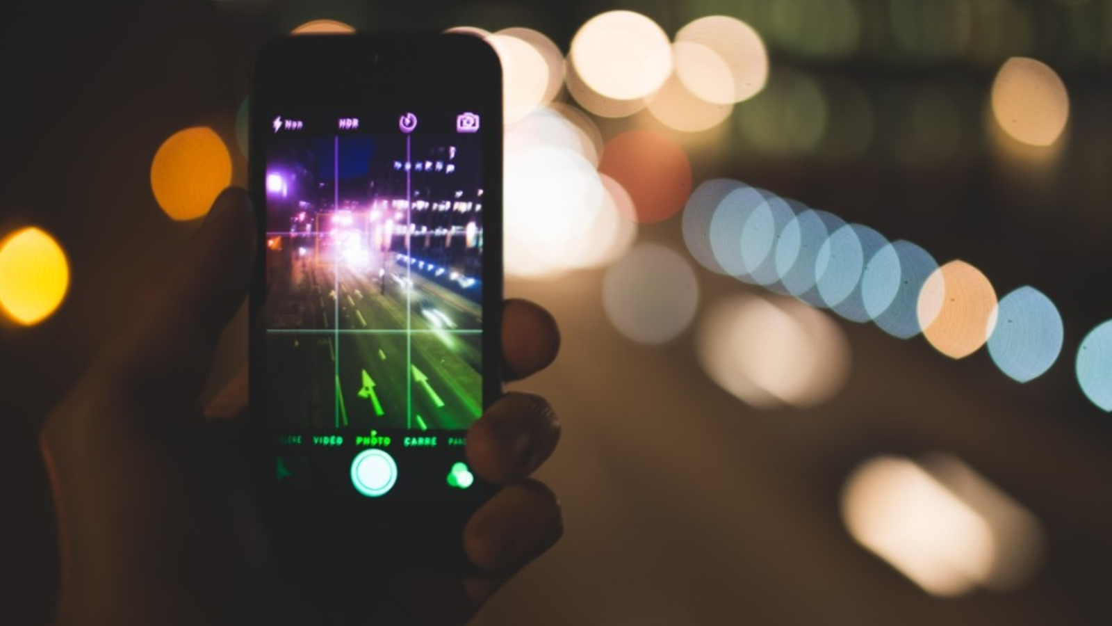 Someone holding an iPhone with camera open, taking a photo of a road at night with bright head lights.