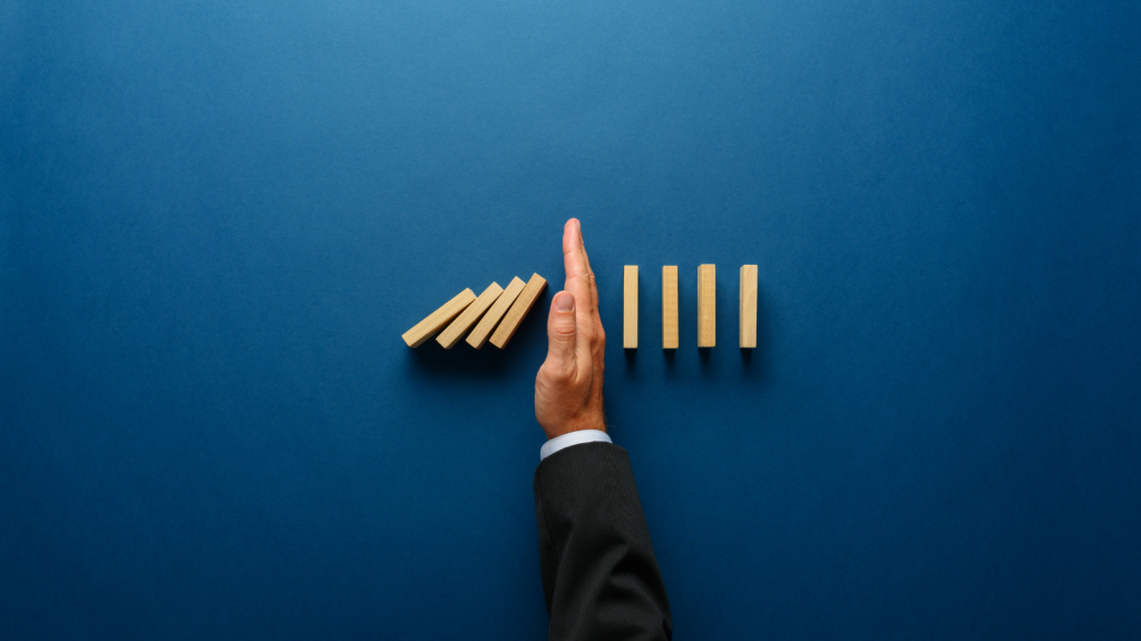 Blue screen, with a hand in a suit stopping a line of dominoes from falling.