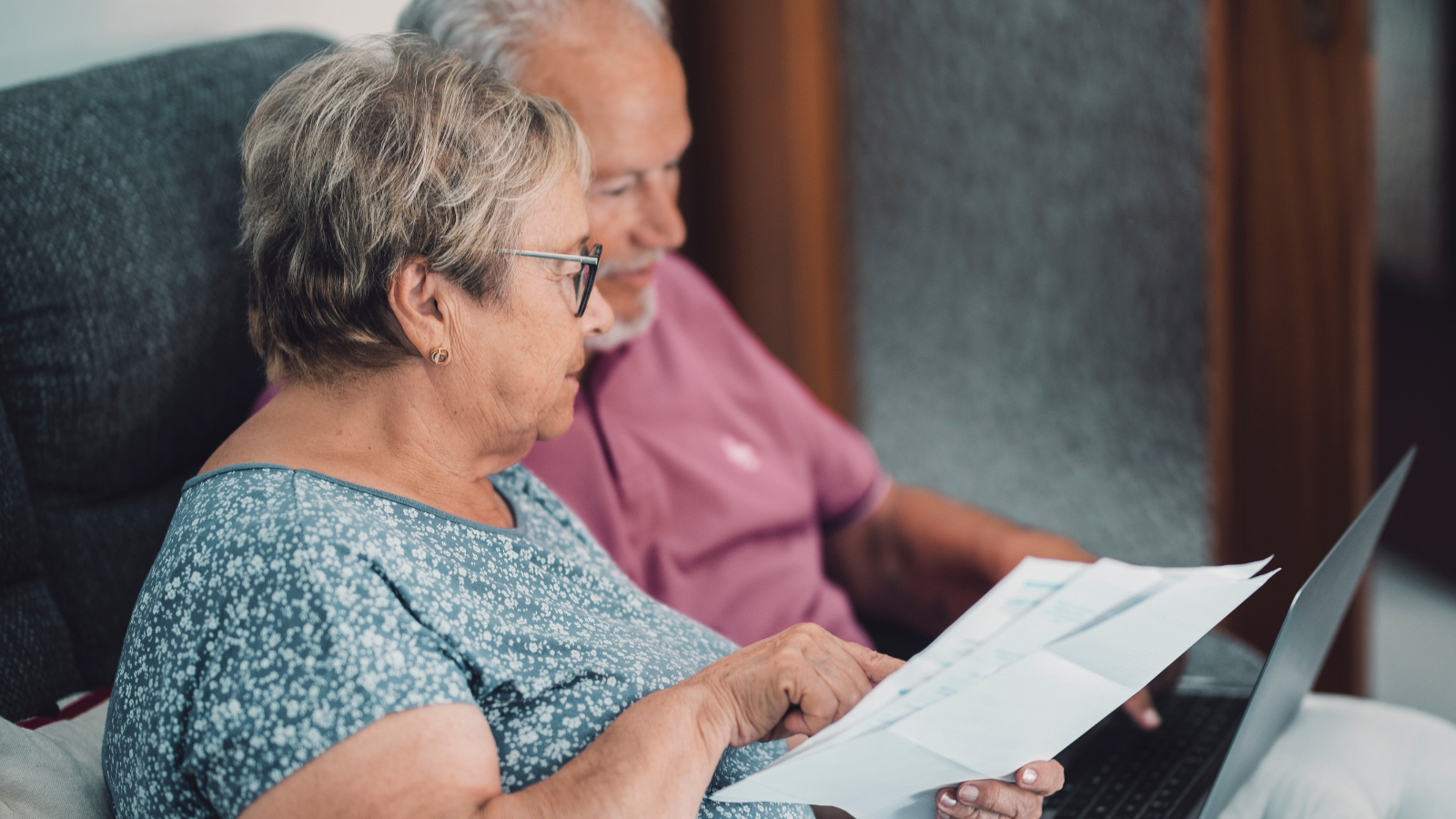 SIde view of real senior couple at home paying bills online with internet banking app and account in cost of living crisis.