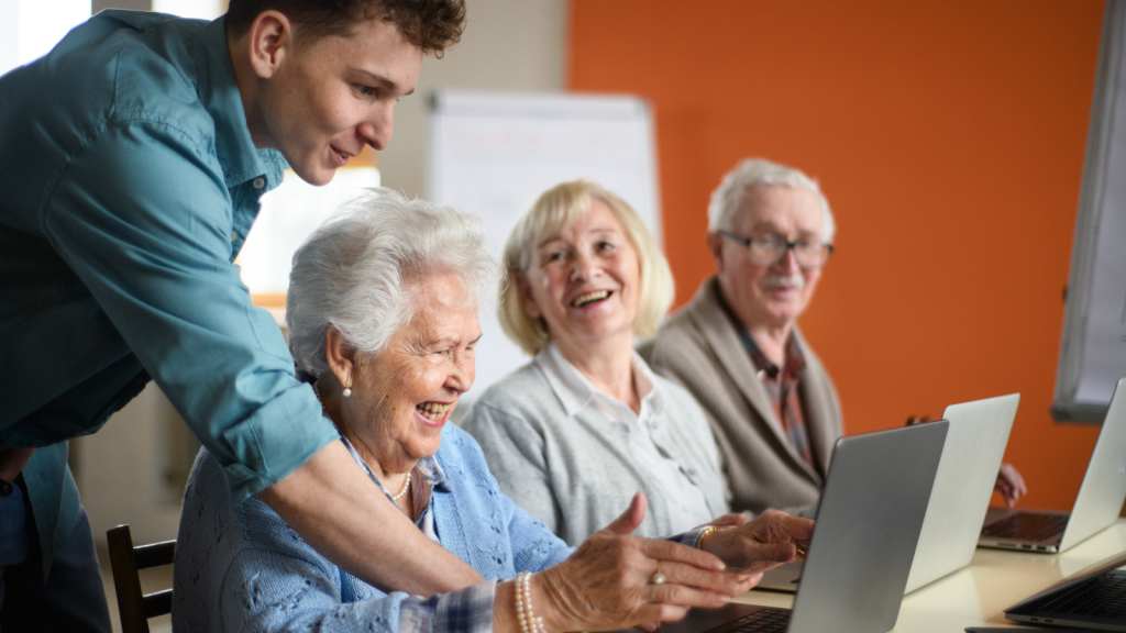 Senior group in retirement home with young instructor learning together in computer class