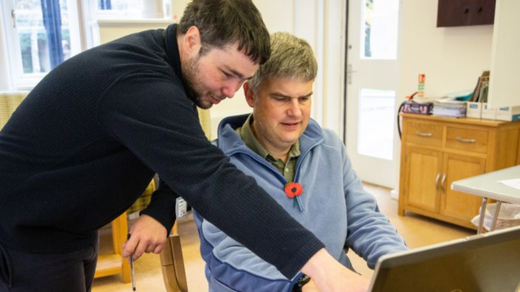 Man helping an older gentleman use a laptop