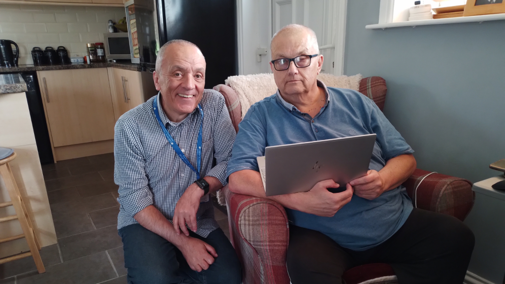 Man supports partially sighted caregiver to set up laptop
