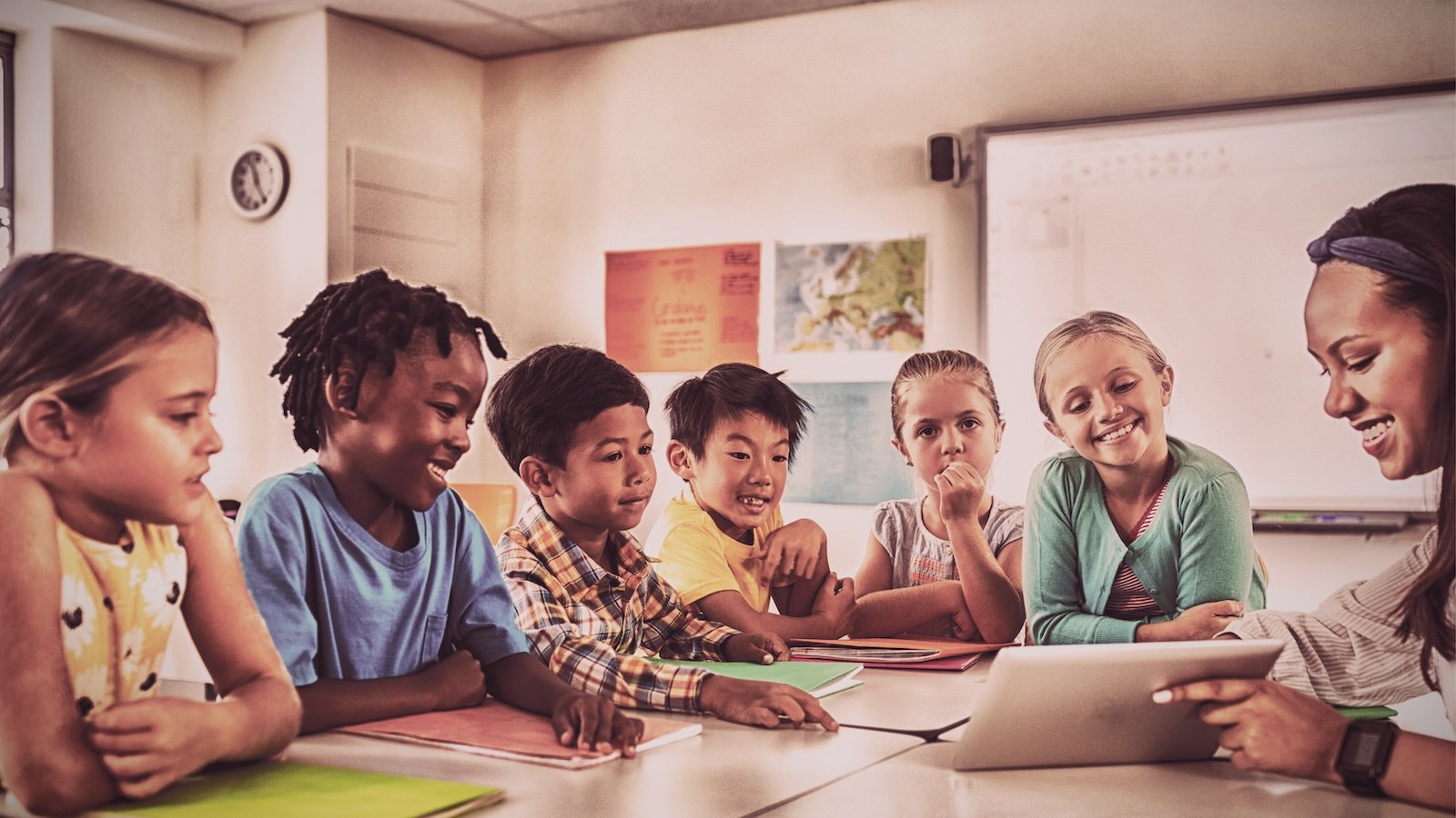 Students at a table with teacher demonstrating how to use a tablet.