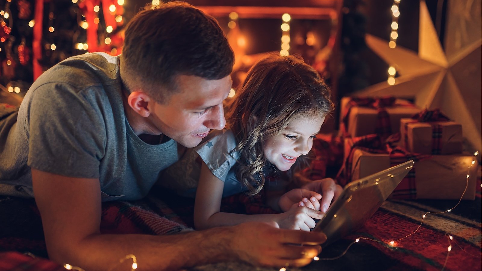 Father and daughter on floor viewing something on a tablet.