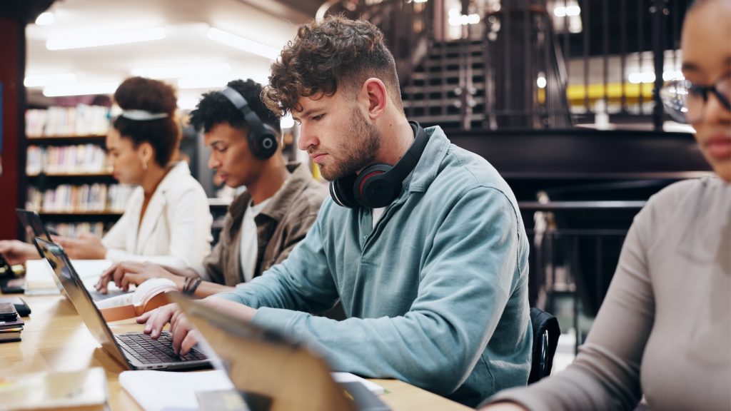 Young man typing on a laptop with headphones resting on his neck.