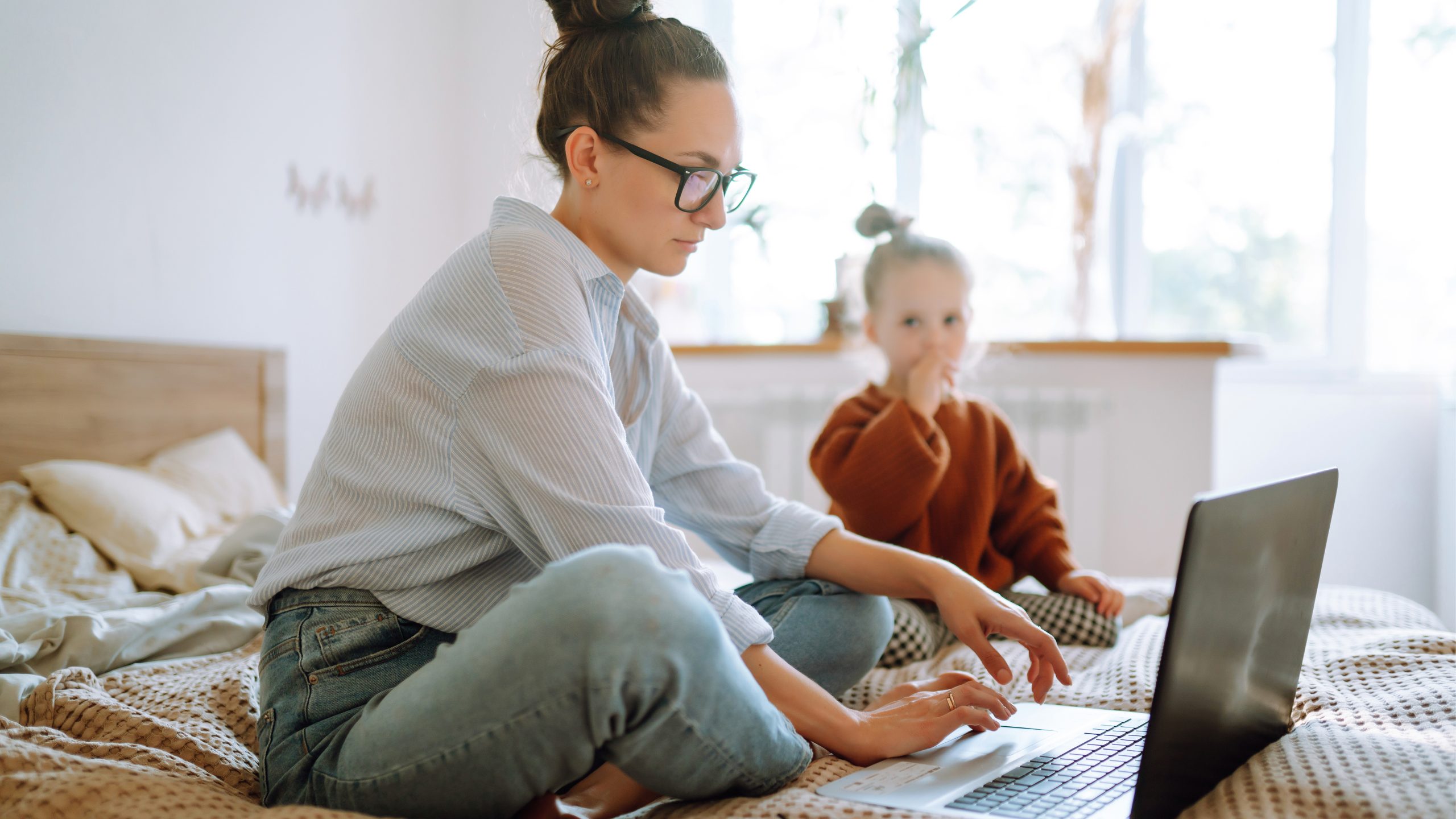 Mother working on laptop with young daughter beside her.